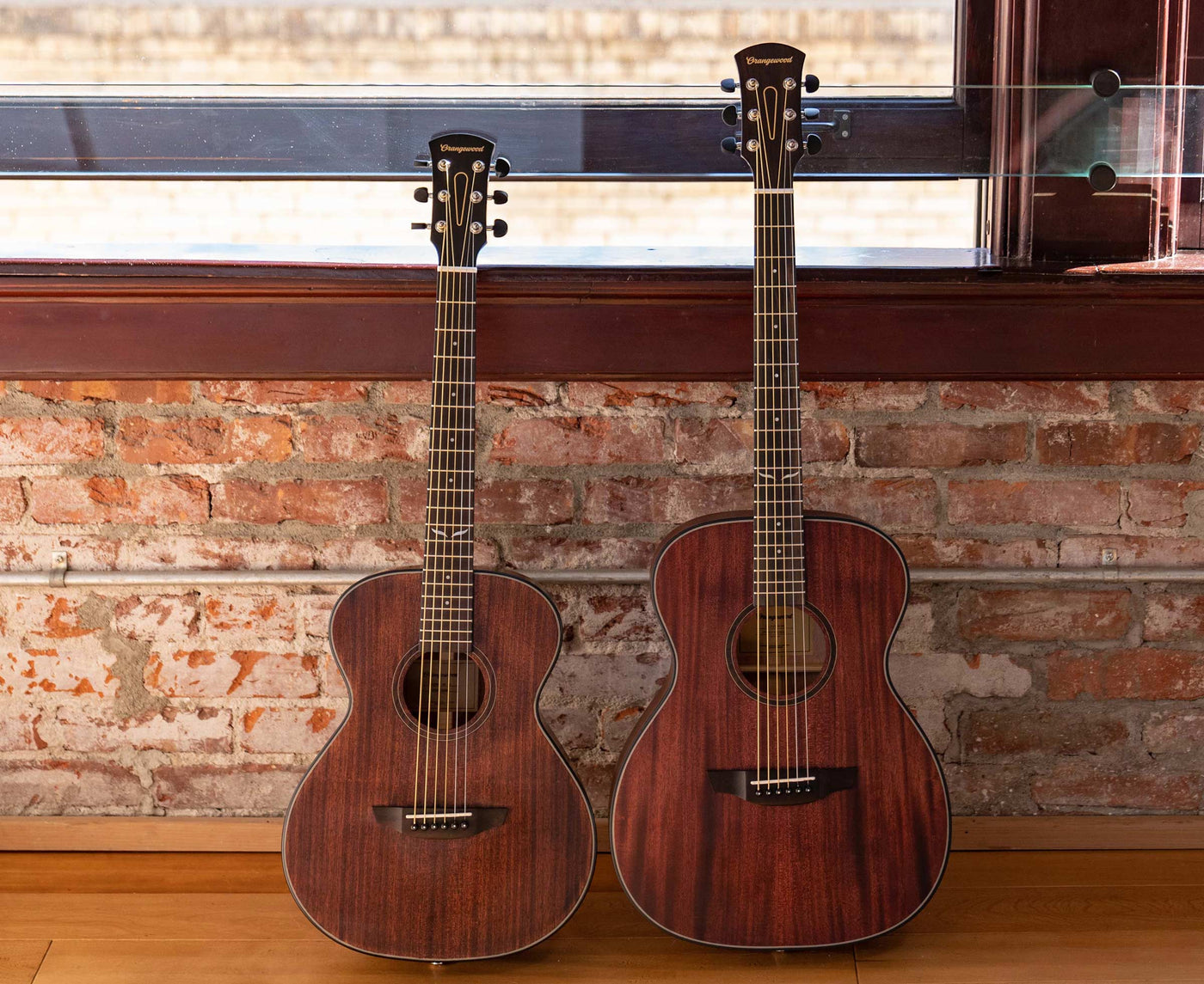 Oliver jr. mahogany guitar and oliver mahogany guitar against a brick wall