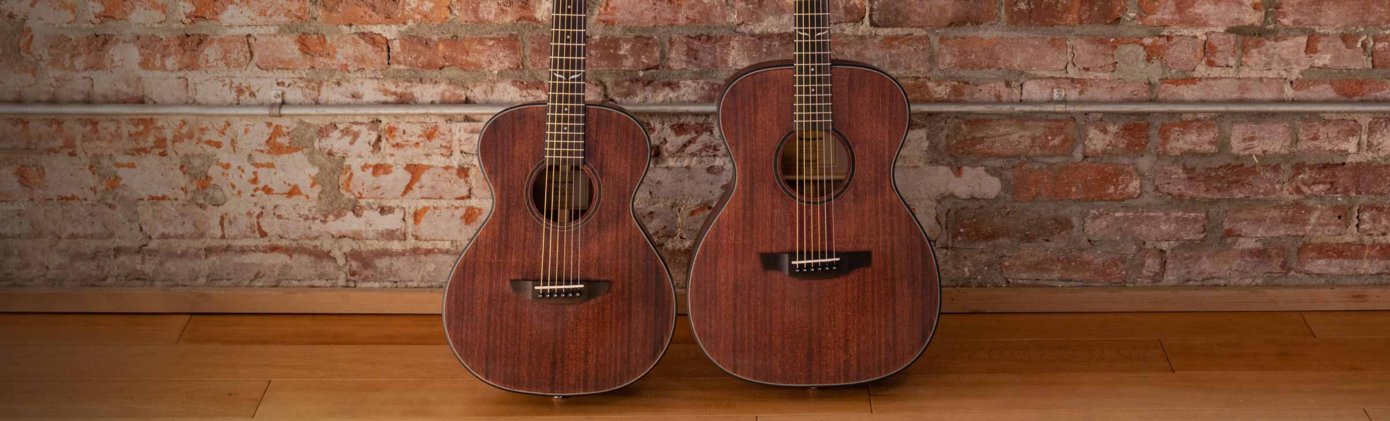 Oliver jr. mahogany and Oliver mahogany guitars against a brick wall