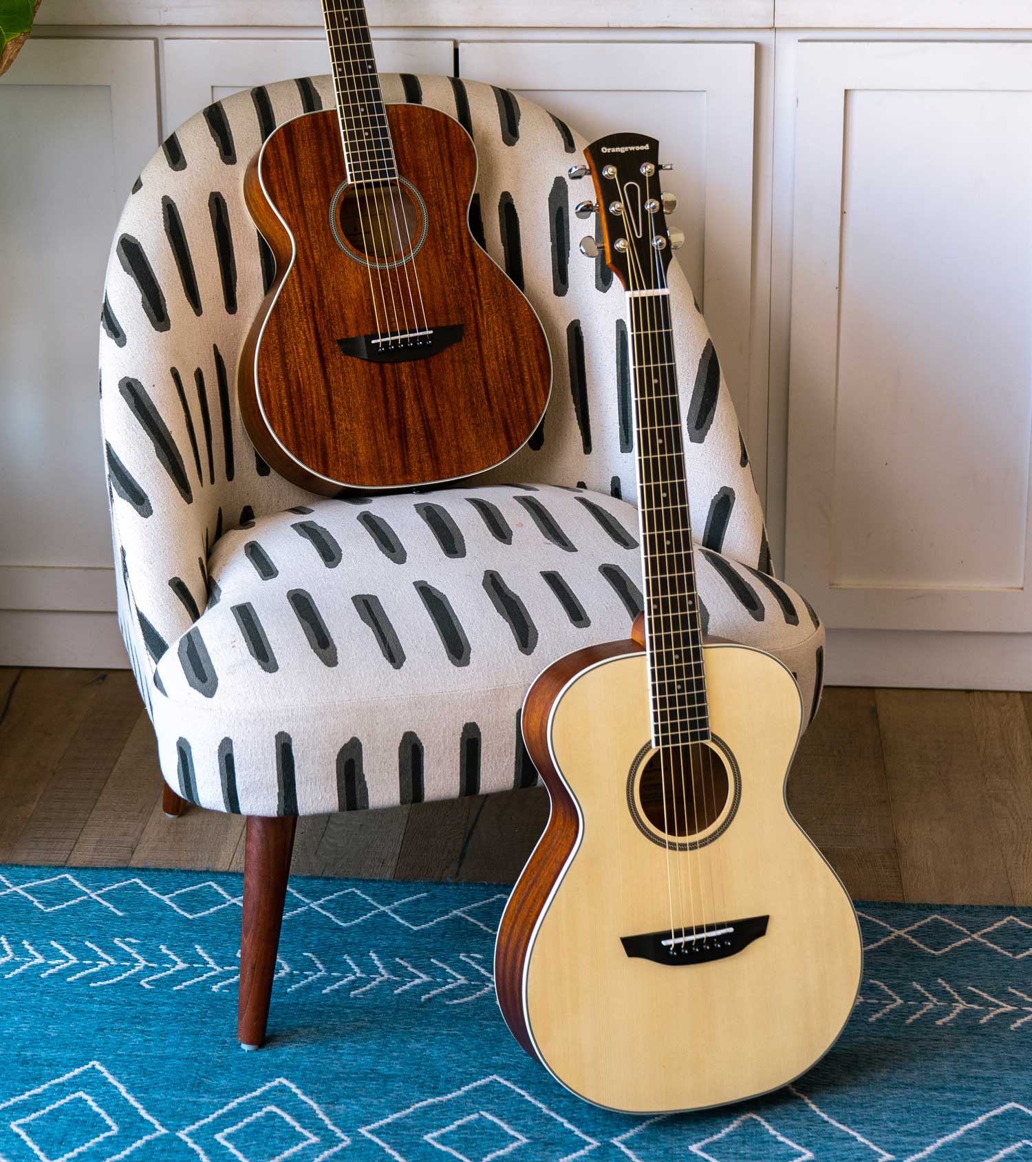 Dana mahogany guitar in a chair and dana spruce guitar on a rug